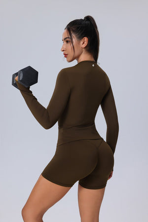 Woman in a #brown athletic outfit lifting a dumbbell against a light gray background
