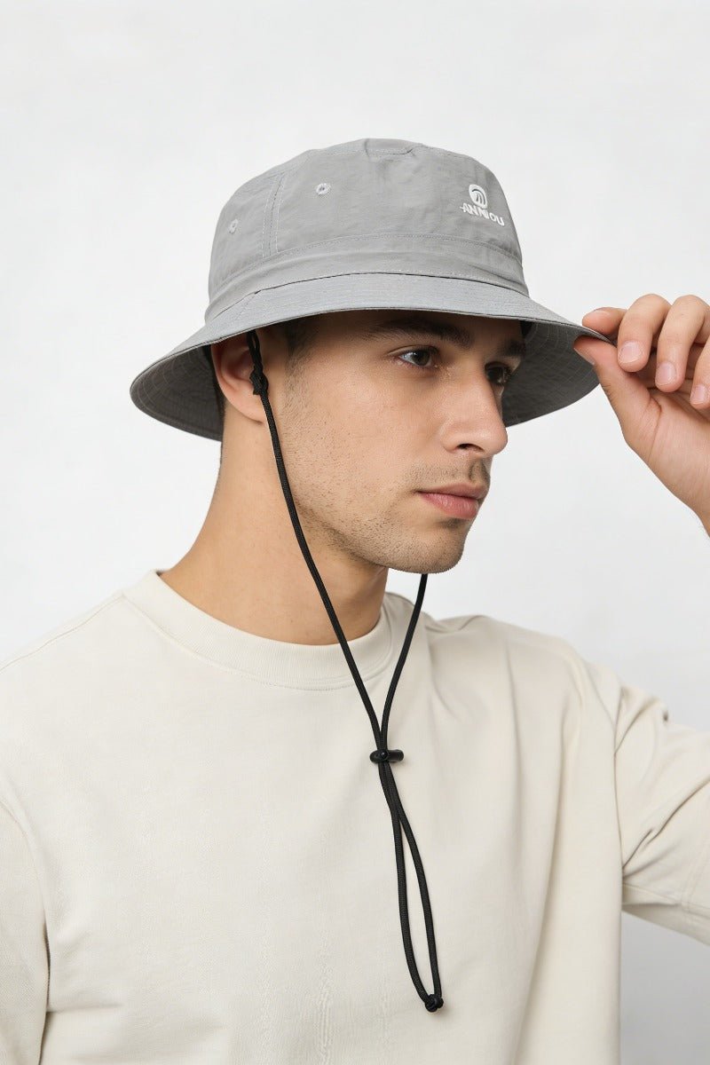 Person wearing a gray bucket hat with a brand logo on a white background