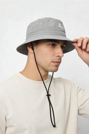 Person wearing a gray bucket hat with a brand logo on a white background