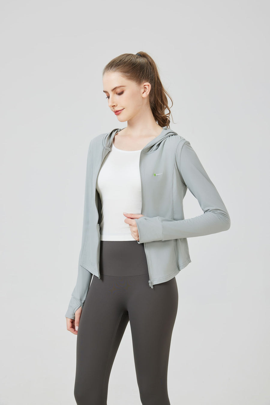 Woman wearing a light gray hoodie and dark gray leggings on a white background. SUN PROTECTION SPORTS HOODED TOP