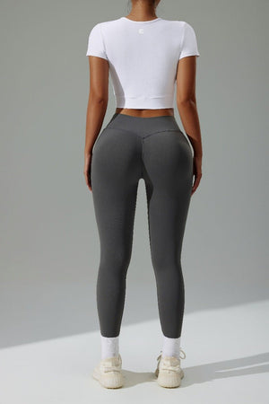 Person wearing gray leggings and a white crop top on a plain background