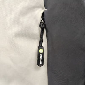 Close-up of a zipper pull tab with the brand name 'ANNIOU' printed vertically in white on a black tab, with a small green circular logo above it. The zipper is shown between two fabric panels, one light gray and one dark gray.