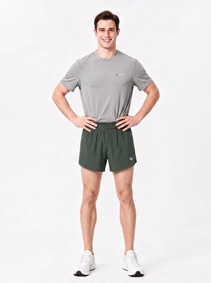 A man stands in a studio wearing a gray short-sleeve athletic T-shirt, army green sports shorts.
