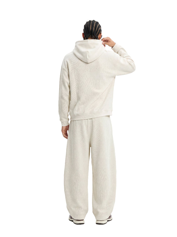 Back view of a male model in an #beige waffle hoodie and matching wide sweatpants against a clean white background.
