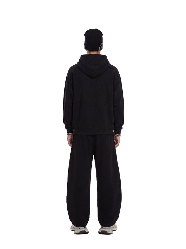 Back view of a male model wearing a #black waffle hoodie and matching wide sweatpants against a plain white background.