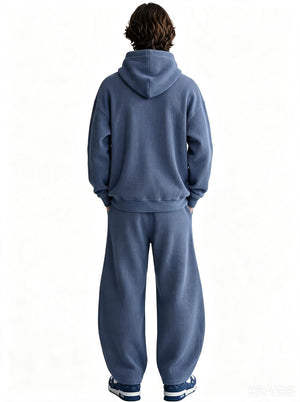 Back view of a male model wearing a blue waffle-knit hoodie and matching wide sweatpants against a plain white background.