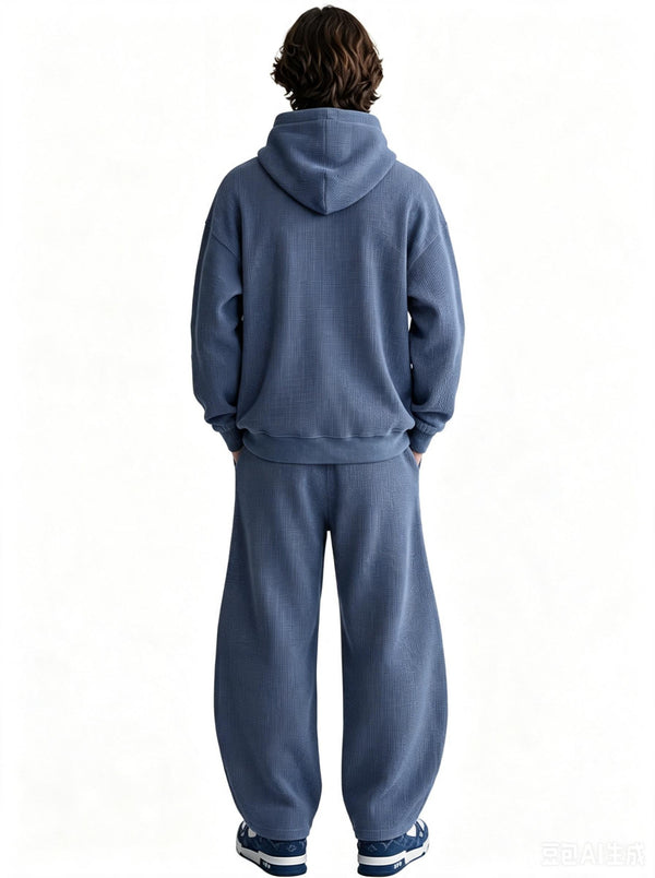 Back view of a male model wearing a blue waffle-knit hoodie and matching wide sweatpants against a plain white background.