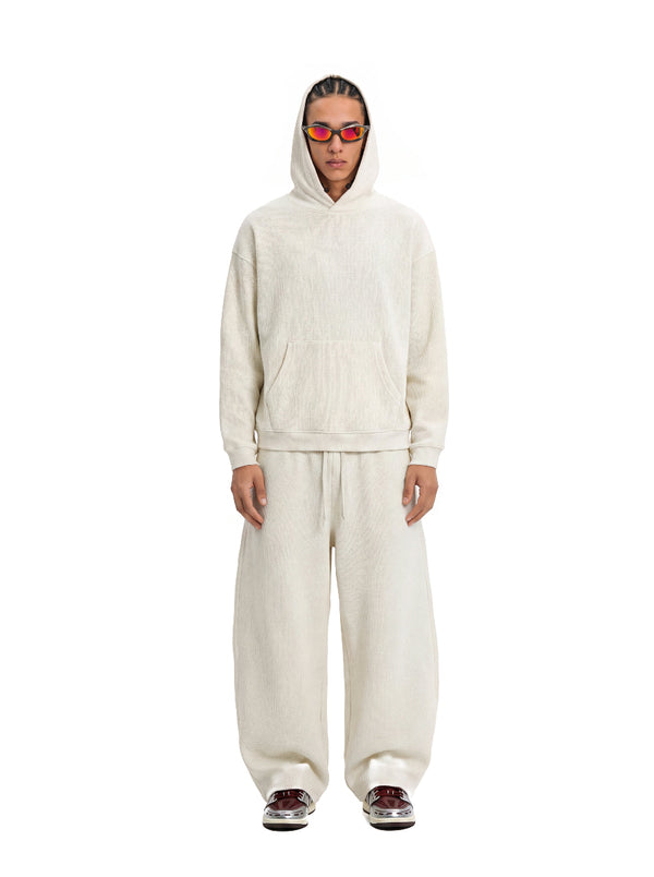 A male model stands front-facing against a plain white background, dressed in an #beige waffle-knit hoodie and matching wide-leg sweatpants.
