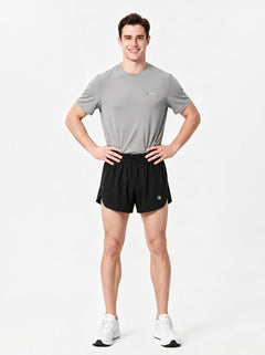 A man stands in a studio wearing a gray short-sleeve athletic T-shirt, black sports shorts.