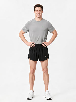 A man stands in a studio wearing a gray short-sleeve athletic T-shirt, black sports shorts.