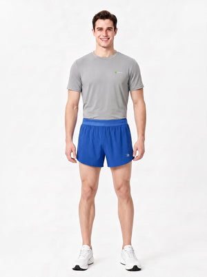 A man stands in a studio wearing a gray short-sleeve athletic T-shirt, blue sports shorts.