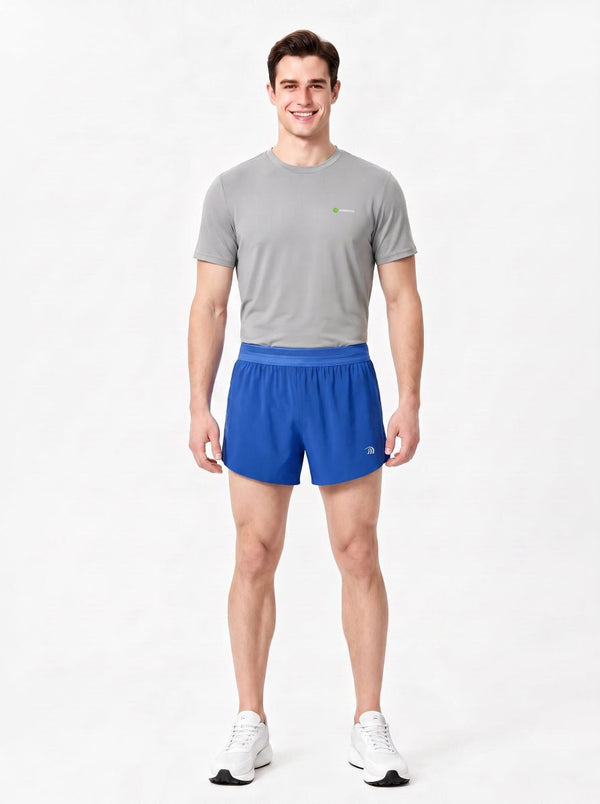 A man stands in a studio wearing a gray short-sleeve athletic T-shirt, blue sports shorts.