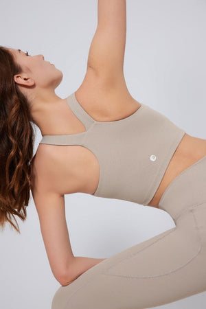 Woman wearing a beige sports bra and leggings against a light gray background