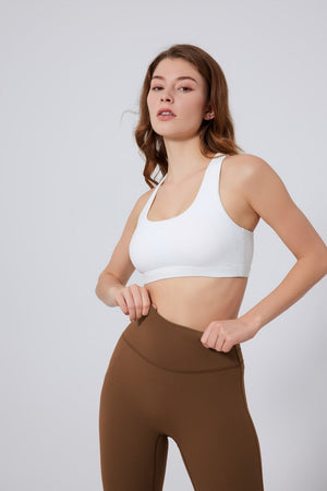 Woman wearing a #white sports bra and brown leggings on a light gray background