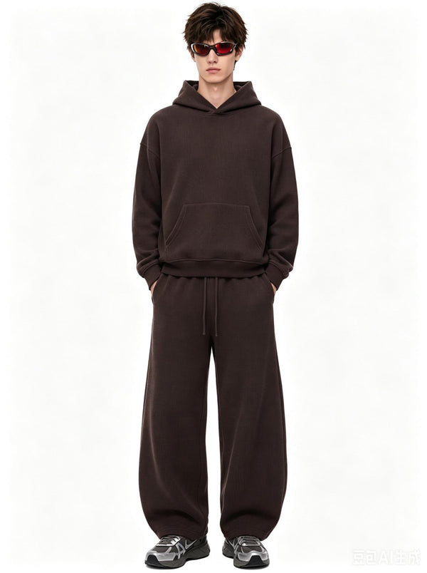 A male model wearing tinted sunglasses stands with hands in pockets against a plain white background, wearing a #Coffee waffle-knit hoodie and matching wide-leg sweatpants.
