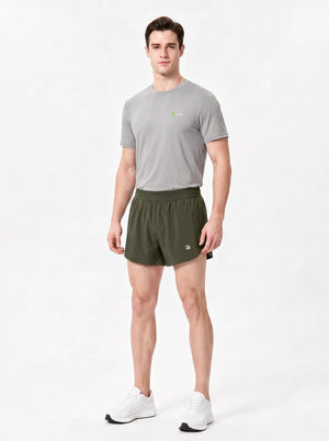 A man stands in a studio wearing a gray short-sleeve athletic T-shirt, dark green sports shorts.