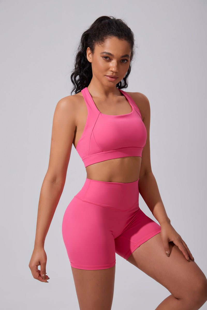 Woman wearing a pink sports bra and shorts set on a gray background