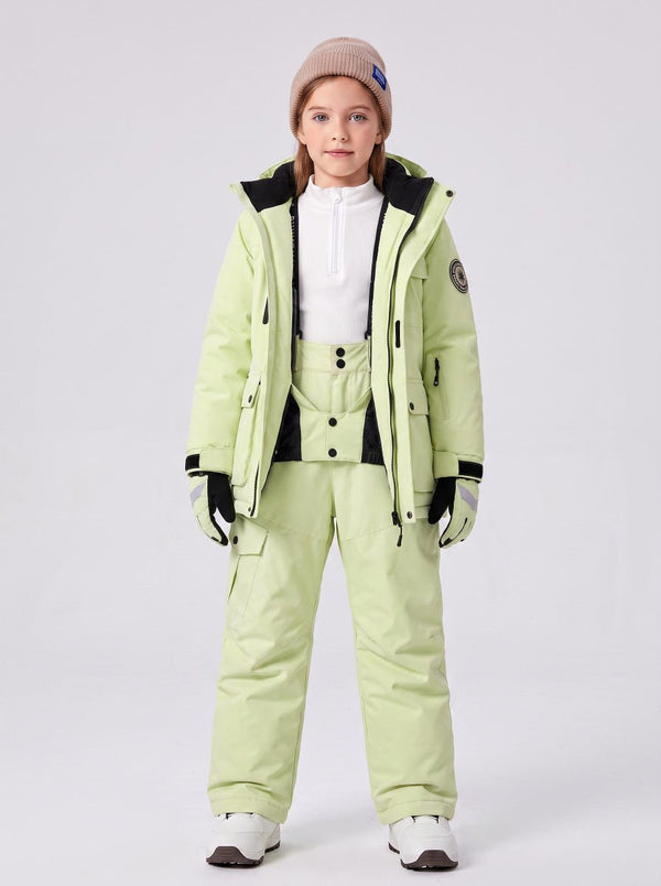 A young girl is wearing a complete #lemonyellow kids ski suit, including a hooded insulated ski jacket and matching suspender snow pants. 