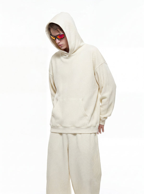 A male model wearing tinted sunglasses and an #beige waffle hooded tracksuit stands against a plain white background in a partial front shot.