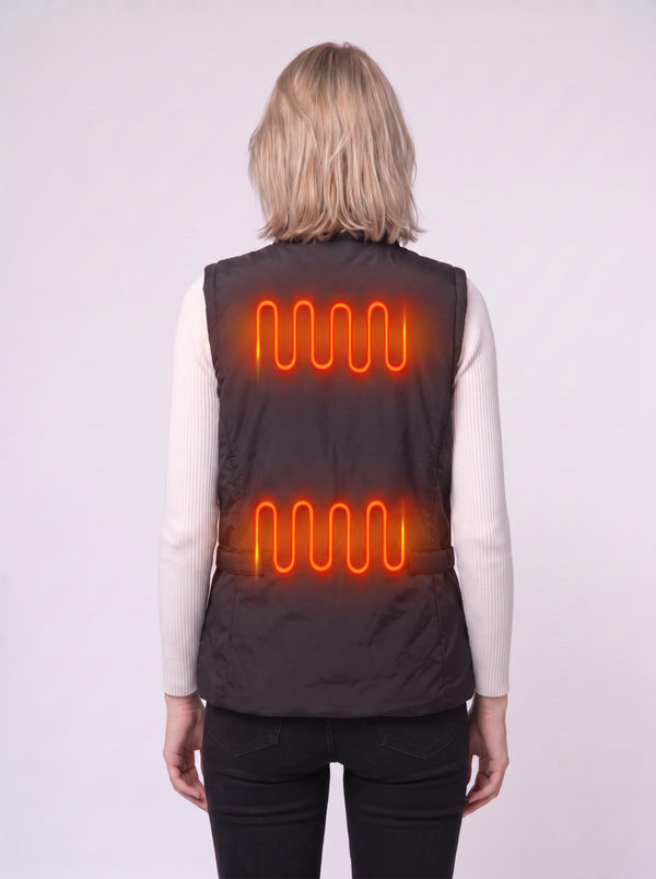 Back‑view shot of a blonde female model wearing a black heated gilet over a white turtleneck top. Bright orange glowing heating‑coil visuals show two heating zones on the vest’s back.