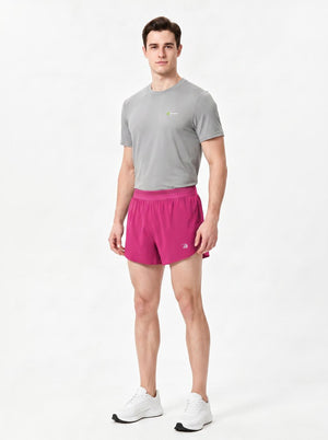 A man stands in a studio wearing a gray short-sleeve athletic T-shirt, rose red sports shorts.