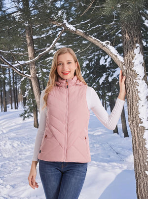 Smiling female model wearing #pink hooded heated gilet, posing in snowy winter pine‑forest outdoor scenery
