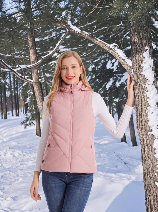 Smiling female model wearing #pink hooded heated gilet, posing in snowy winter pine‑forest outdoor scenery