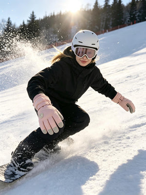 Young female snowboarder in black winter suit, white helmet and ski goggles carves down sun‑lit snowy slope, wearing #pink warm ski gloves, snow sprays around her, pine trees in background.