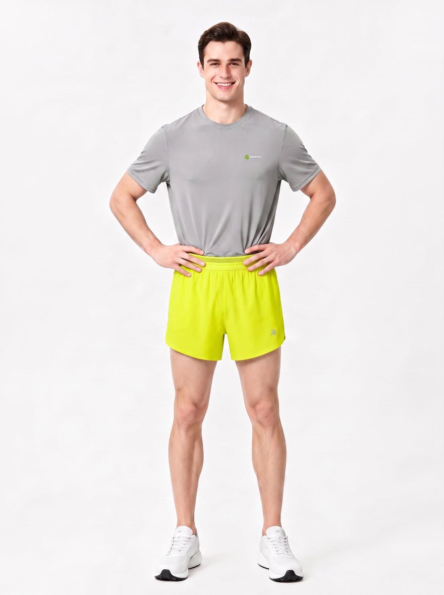 A man stands in a studio wearing a gray short-sleeve athletic T-shirt, bright yellow-green sports shorts.