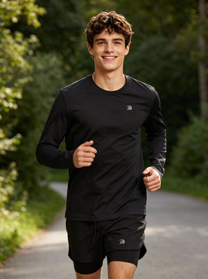 A male runner wearing a #black long-sleeve athletic shirt and black shorts jogs on a tree-lined road. The shirt features a small reflective logo on the left chest, highlighting a lightweight, breathable running top for outdoor sports and training.