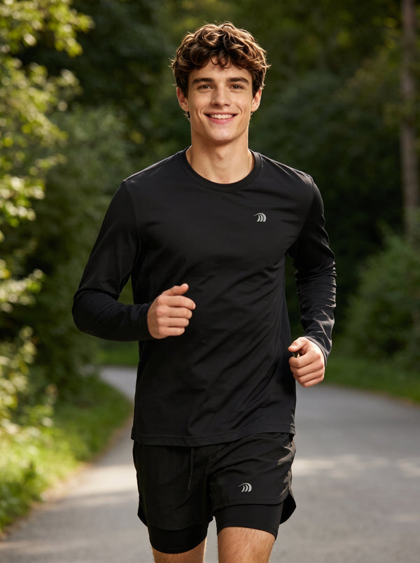 A male runner wearing a #black long-sleeve athletic shirt and black shorts jogs on a tree-lined road. The shirt features a small reflective logo on the left chest, highlighting a lightweight, breathable running top for outdoor sports and training.