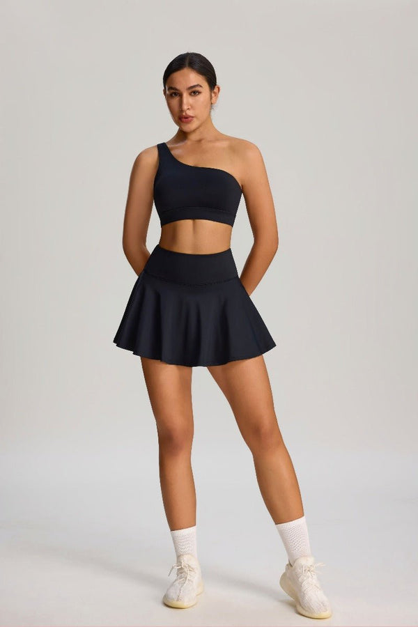 Woman wearing a #black one-shoulder sports bra and skirt with white sneakers 
