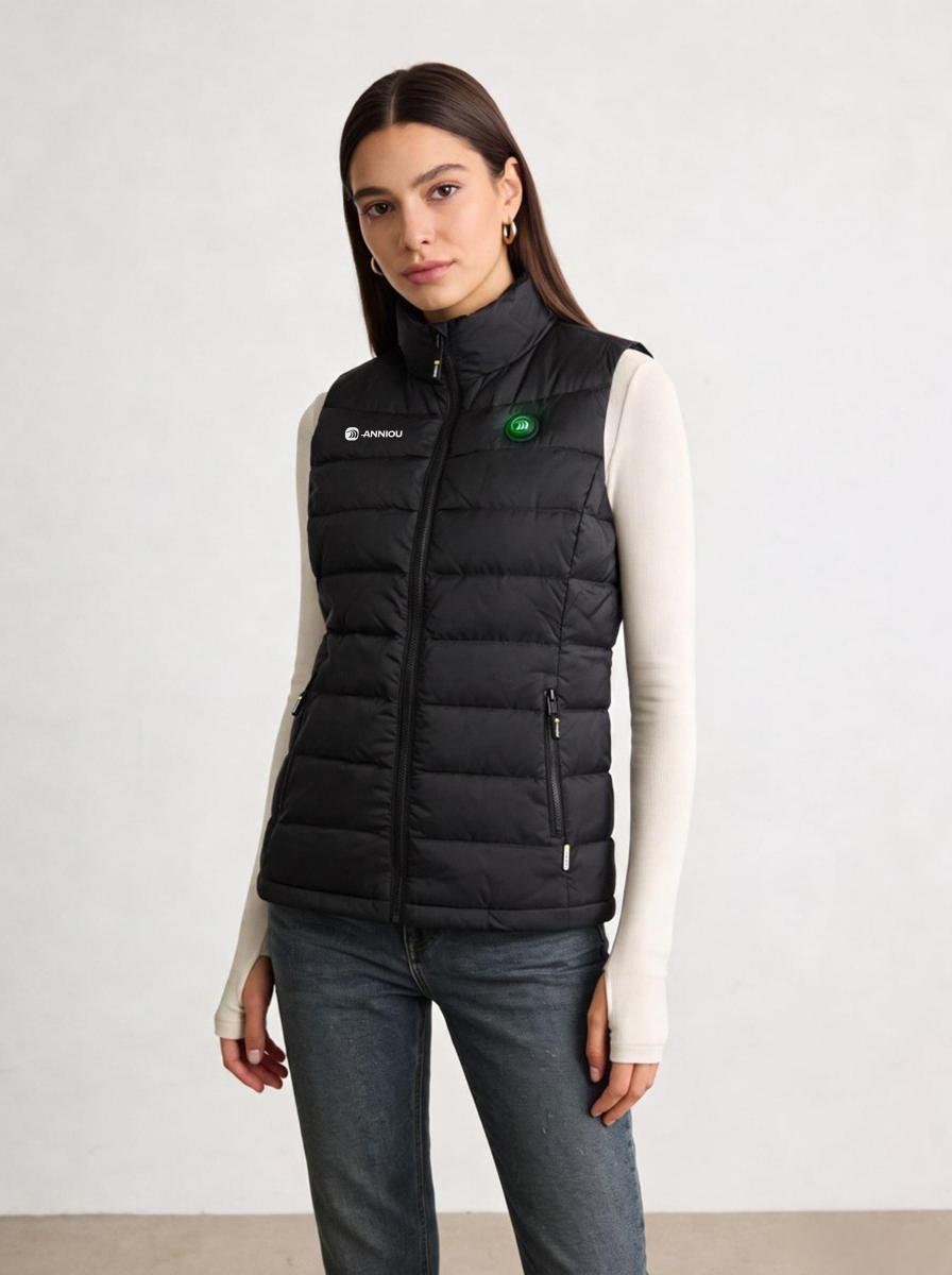 A young woman modeling a black heated puffer vest over a cream long-sleeve top and blue jeans.