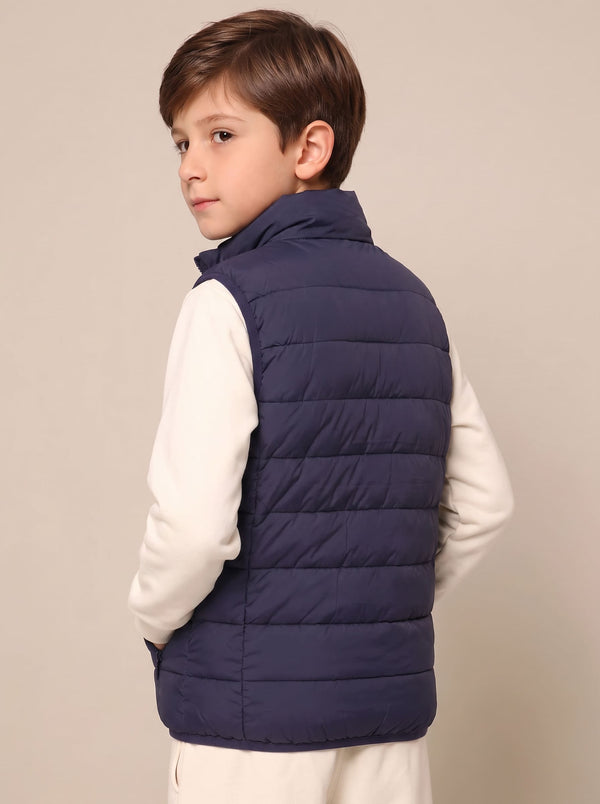A young boy wearing a navy blue quilted puffer heated vest over a cream-colored long-sleeve shirt.