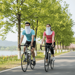 Two people riding bicycles on a path with trees and a lake in the background. Both wearing uv masks