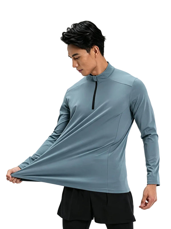 A male model stretches the hem of a #grey blue half-zip long-sleeve athletic top against a plain white background to show fabric elasticity.