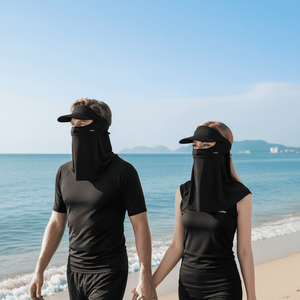 Two people wearing black sun visors and face coverings on a beach.