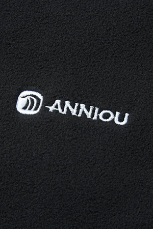 Close-up of a black fabric with 'Anniou' logo embroidered in white.