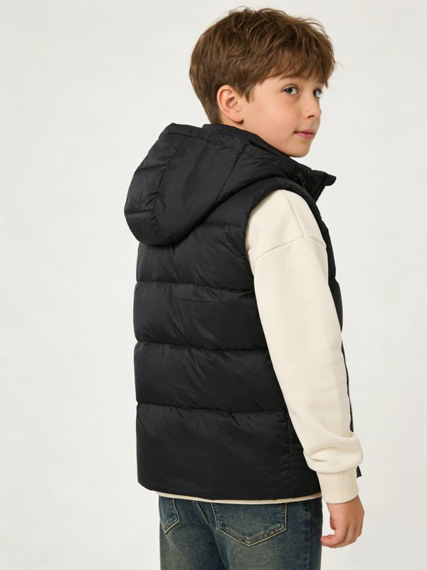 A young boy wearing a black heated hooded puffer vest photographed from the back.
