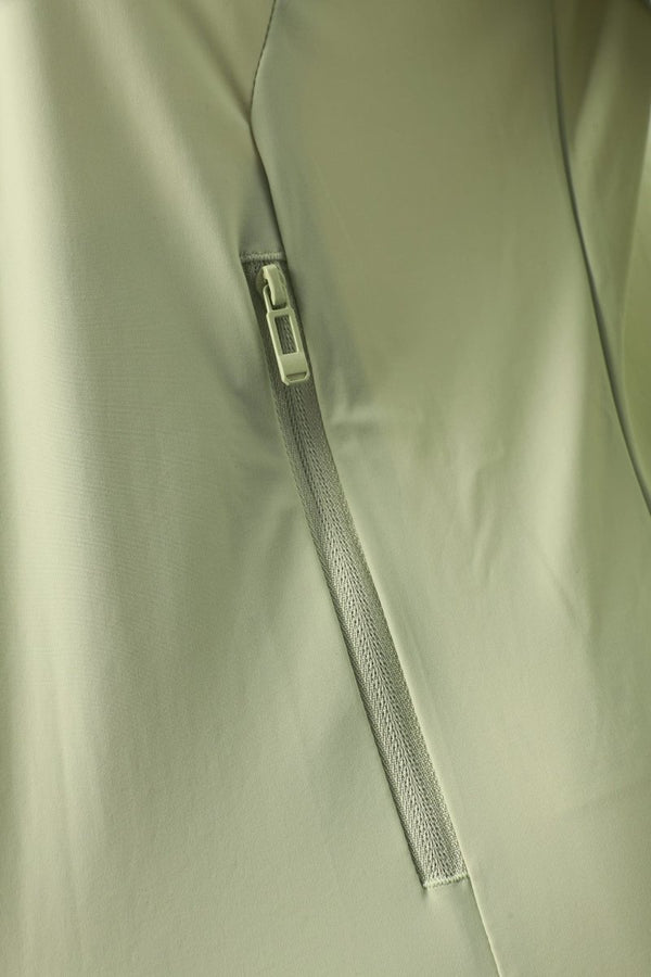 Close-up of a light sage green or gray-green fabric jacket with a vertical zippered pocket and a silver zipper pull.