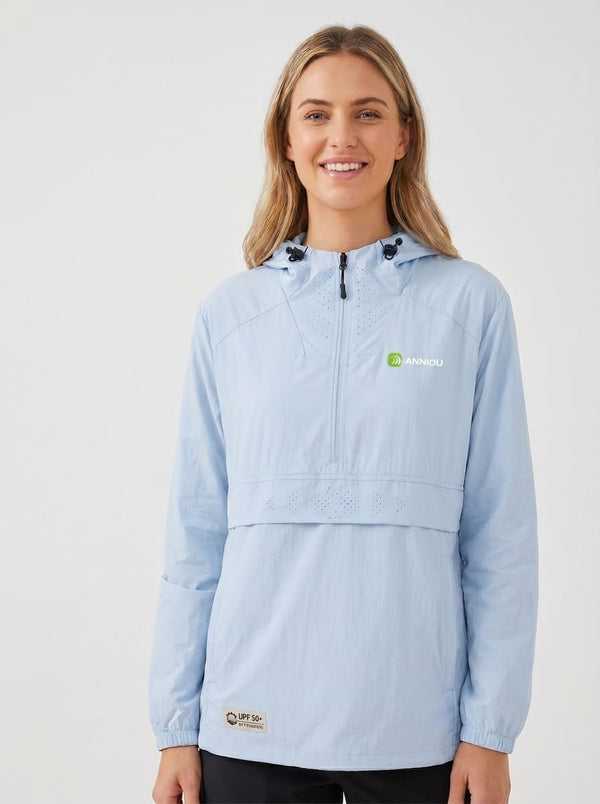 A woman wearing a #lightblue hooded UV jacket with a half-zip front, featuring a green and white 'Aimou' logo on the left chest and a small beige patch near the hem, set against a plain light gray studio background.