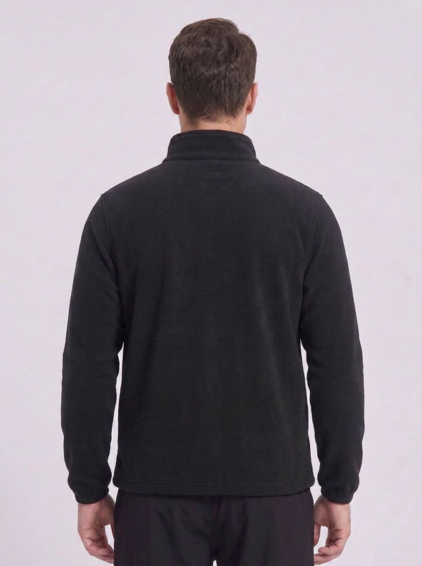 A man viewed from the back wearing a black long-sleeve quarter-zip fleece pullover and dark trousers, set against a plain light gray studio background.