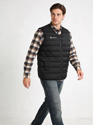 A man wearing a #black heated puffer vest over a beige and brown plaid flannel shirt, paired with blue jeans, photographed against a plain white studio background.