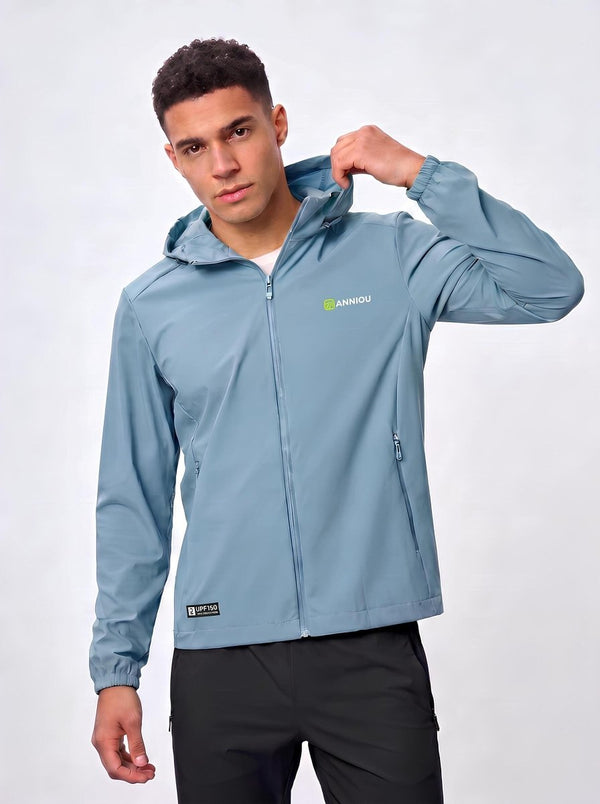 A man wearing a light #blue hooded jacket with a full zipper and a small green and white 'AINHIDU' logo on the left chest, paired with black pants, against a light gray studio background.