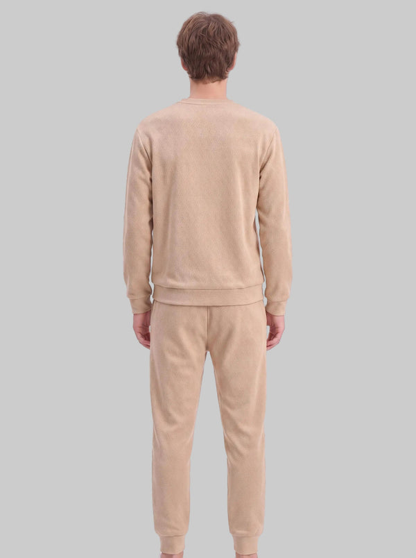 A male model shows the back view of a khaki two-piece tracksuit. The sweatshirt and jogger pants are crafted from diamond jacquard textured fabric. It features a crew neck sweatshirt with ribbed hem and cuffs, paired with matching tapered jogger trousers with ribbed ankle cuffs. 