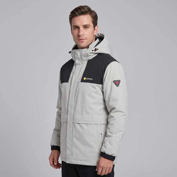 Studio portrait of European male model in #gray men's heated hooded jacket, wind-resistant thermal outdoor winter coat with brand logo and arm patch, solid light grey background, apparel product photography