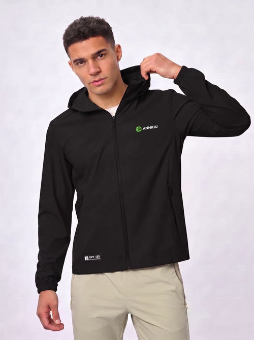 A man wearing a #black zip-up hooded jacket with a green and white 'ANIMOU' logo on the left chest, paired with beige pants, against a light gray studio background.