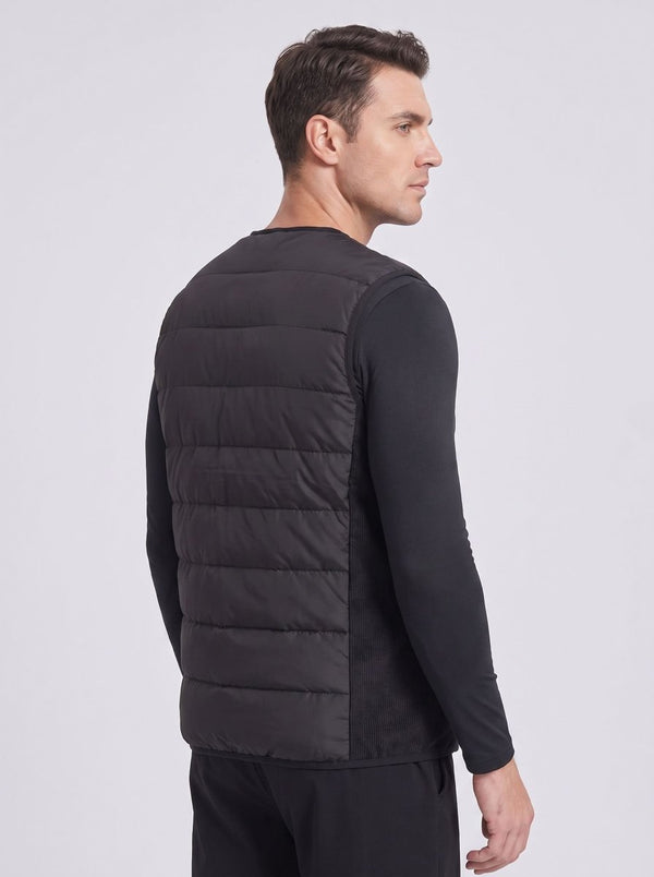 A man shown from the back side wearing a black quilted heated puffer vest over a black long-sleeve shirt.