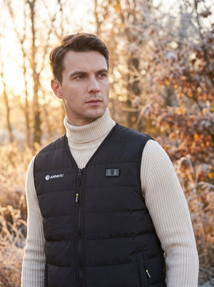 A man wearing a black puffer vest over a cream ribbed turtleneck sweater, standing outdoors in a softly blurred autumn forest setting. The vest has a visible white 'ANNOU' logo on the left chest.