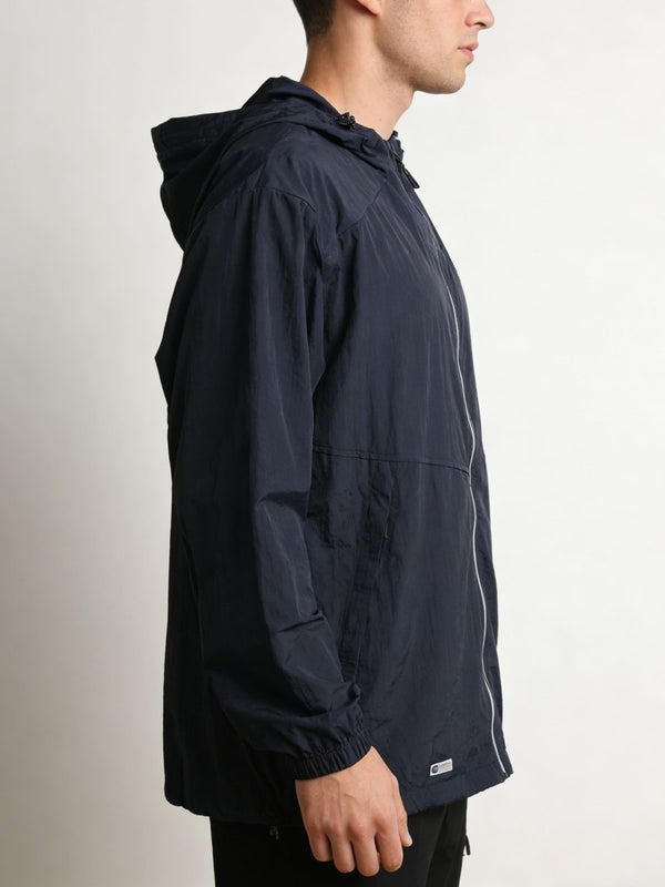 A man shown in profile wearing a dark #navy hooded jacket with a front zipper and a small white logo patch near the hem, photographed against a plain light background.